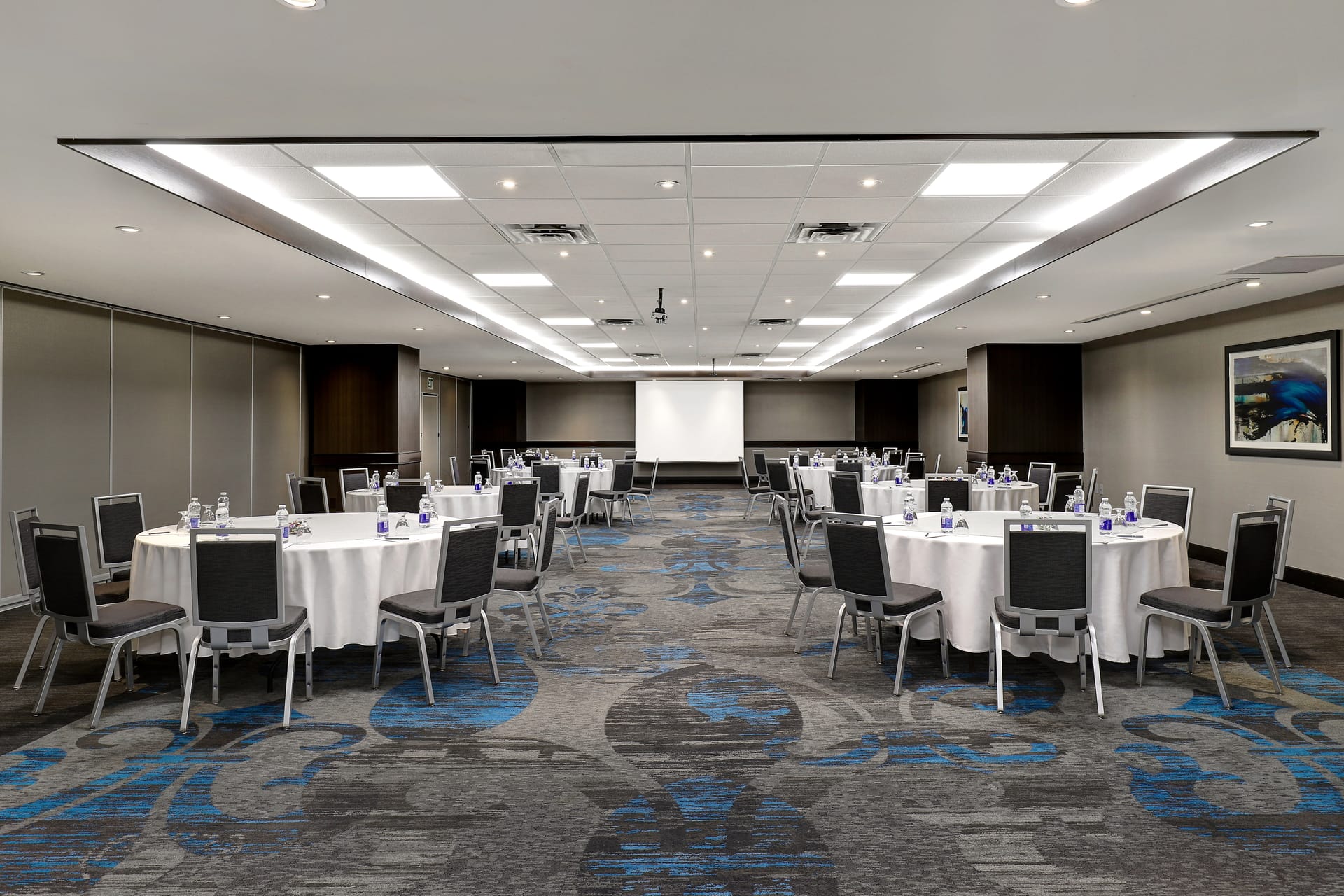 Large conference room with circle table, white linen, modern carpet and a large projection screen.