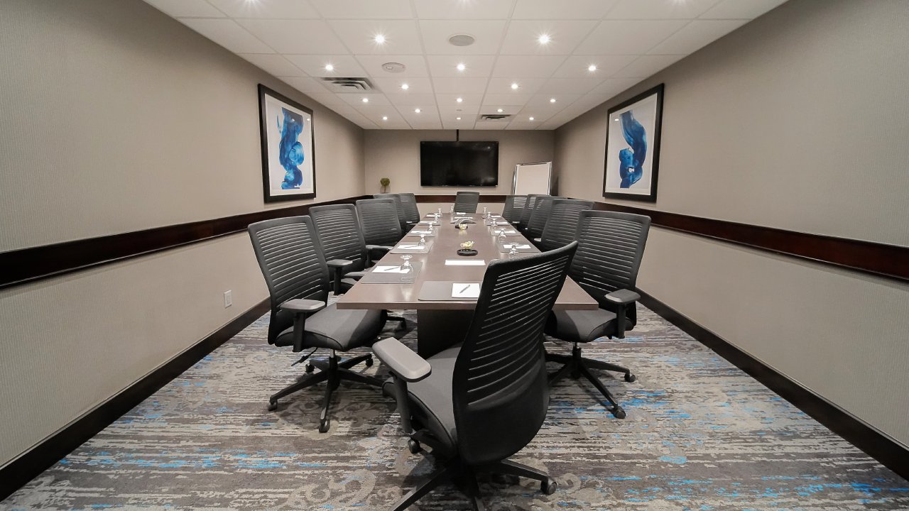 Large bright conference meeting room with large conference table with seating for twelve. A large television is at the end of table with modern art on the wall.